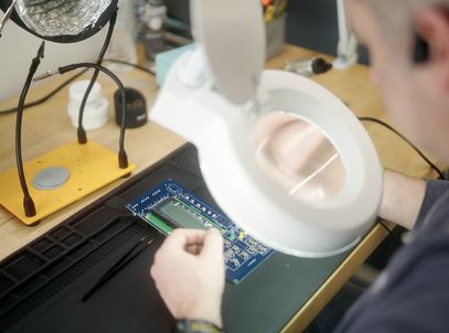 Engineer inspecting a circuit board under a lighted magnifier
