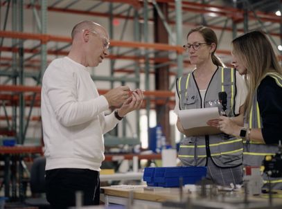 Engineers in safety vests reviewing a part on a manufacturing floor